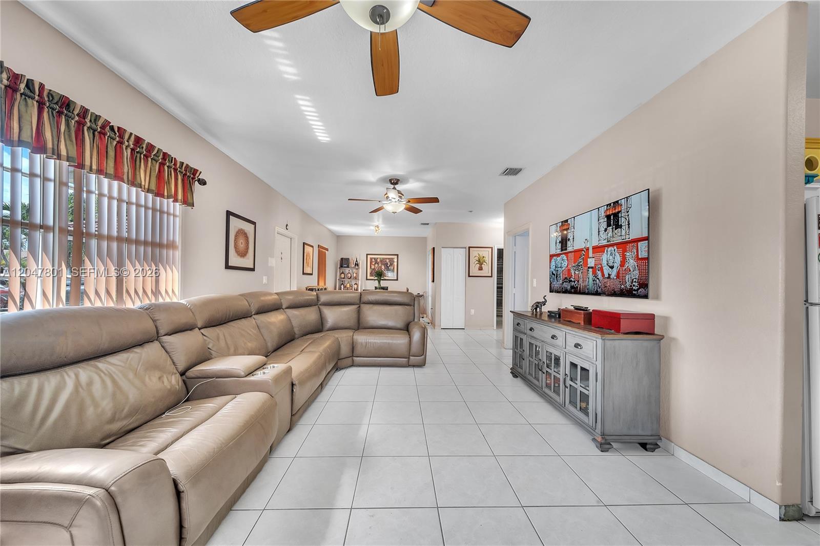 A living room features a large tan sectional sofa, tile flooring, and a wall-mounted television — 7565 N Augusta Dr # 7567, Hialeah FL 33015, HIALEAH, FL