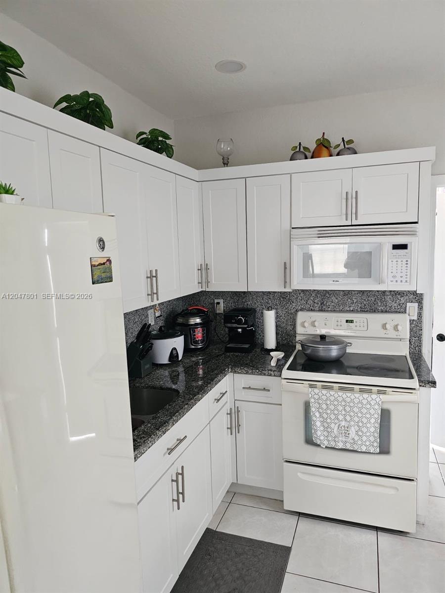 A kitchen features white cabinets, granite countertops, and white appliances — 7565 N Augusta Dr # 7567, Hialeah FL 33015, HIALEAH, FL