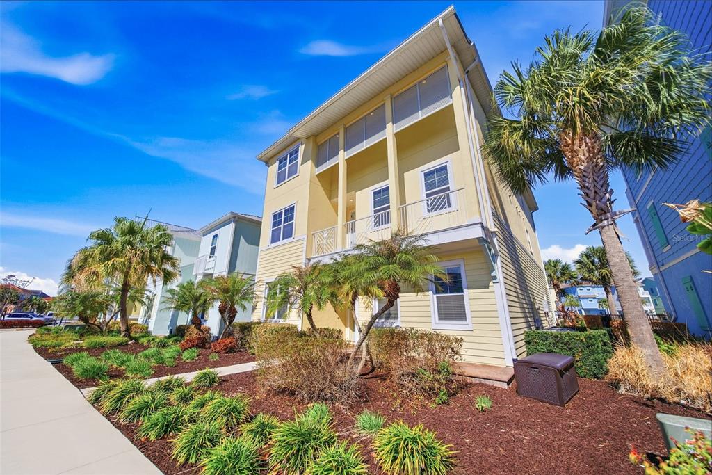 A three-story yellow house with a balcony and palm trees in the front yard — 8017 SURF STREET, KISSIMMEE, FL