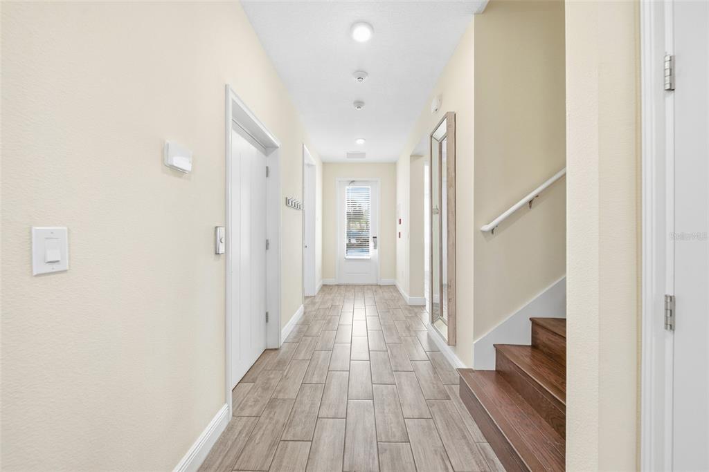 A hallway with wood-look tile flooring, a staircase, and a door leading to the outside — 8017 SURF STREET, KISSIMMEE, FL