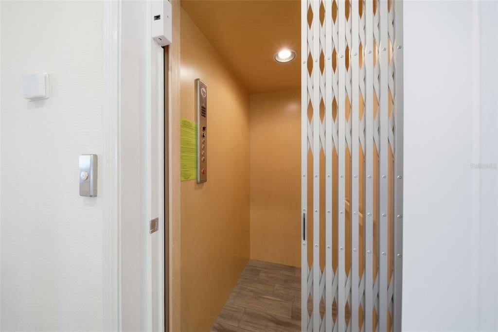 An indoor residential elevator with a collapsible metal gate and wood-paneled interior — 8017 SURF STREET, KISSIMMEE, FL