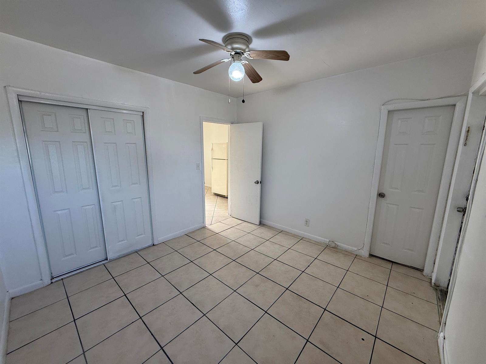 An empty room with white walls, tile flooring, a ceiling fan, and three white doors — 6014 Fillmore Street # 4e, Hollywood FL 33024, HOLLYWOOD, FL