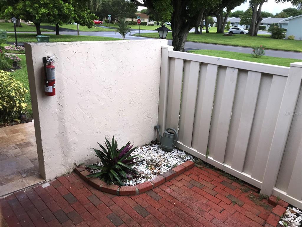 A brick patio features a small garden bed, a white privacy wall, and a fire extinguisher — 3705 34TH AVE DRIVE W, BRADENTON, FL