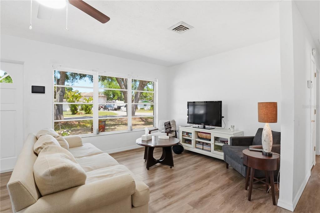 A living room features light wood-look flooring, a beige sofa, a television, and large windows — 73 SAINT LUCIE AVENUE, SARASOTA, FL