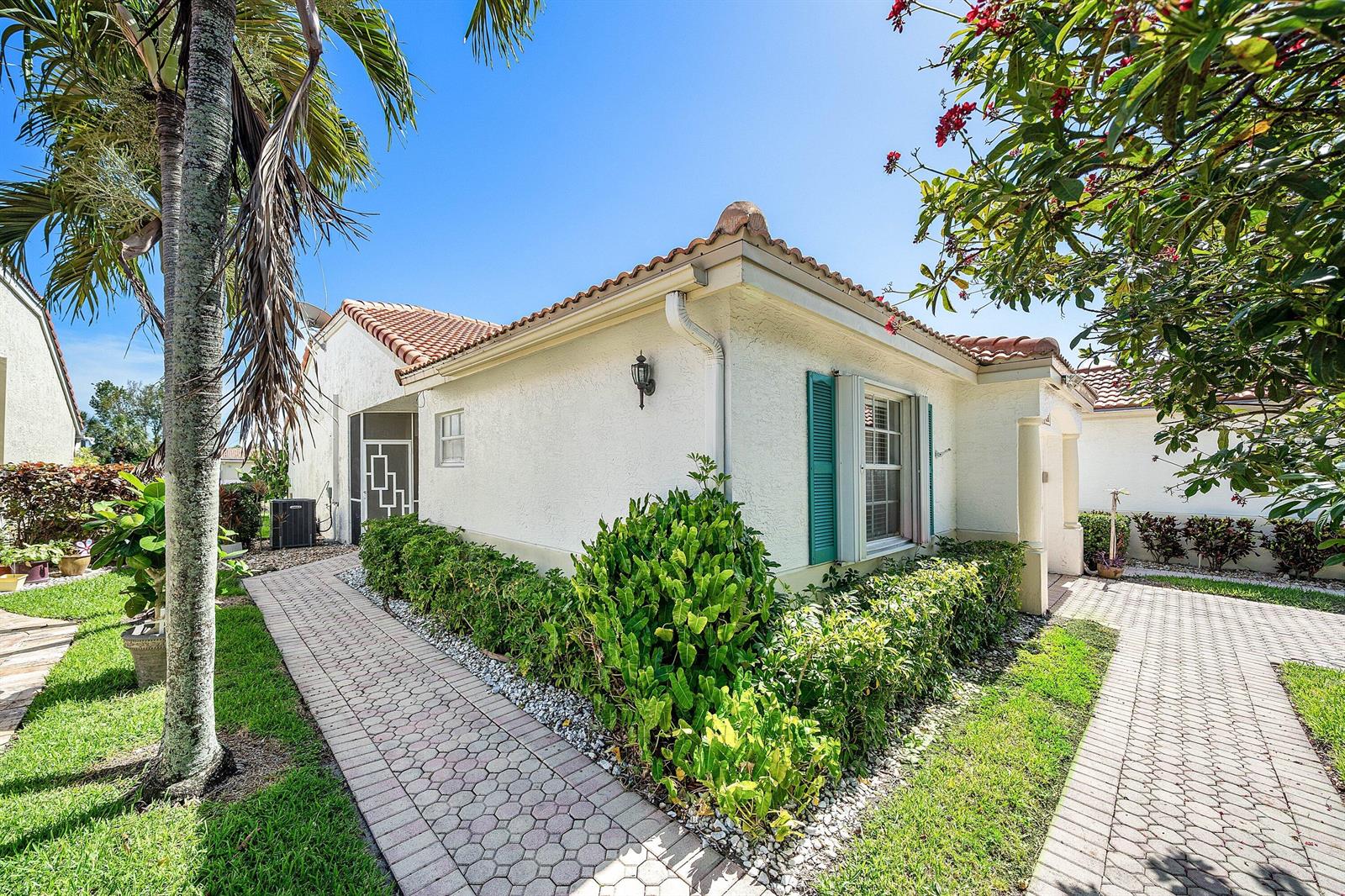 A stucco house exterior features a tiled roof, teal shutters, and a paved walkway — 6192 Floral Lakes Drive, Delray Beach FL 33484, DELRAY BEACH, FL