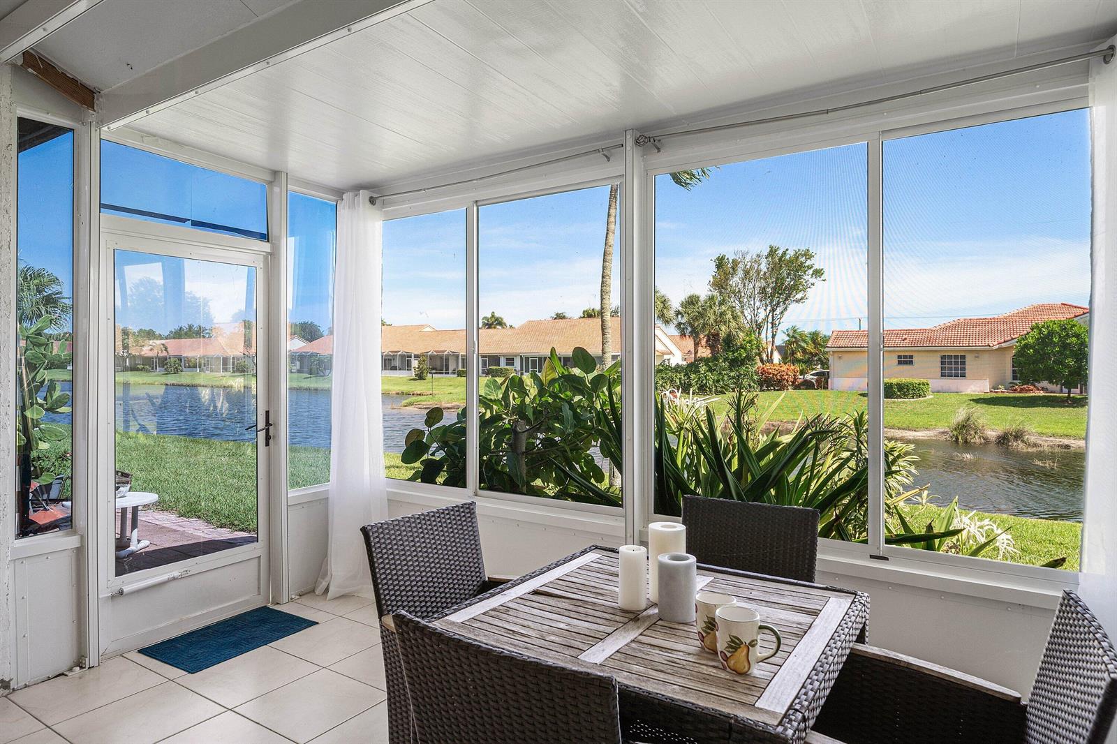 A sunroom with tile floors, wicker furniture, and large windows overlooking a lake and houses — 6192 Floral Lakes Drive, Delray Beach FL 33484, DELRAY BEACH, FL