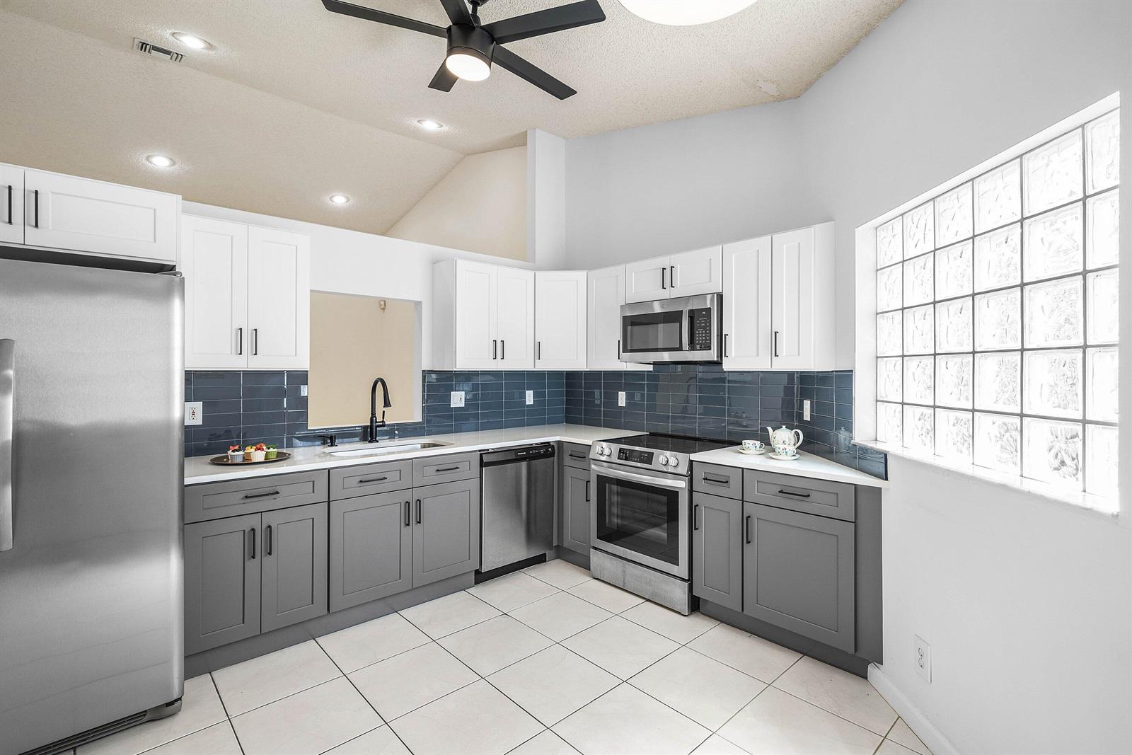 A kitchen features white upper cabinets, gray lower cabinets, stainless steel appliances, and glass blocks — 6192 Floral Lakes Drive, Delray Beach FL 33484, DELRAY BEACH, FL