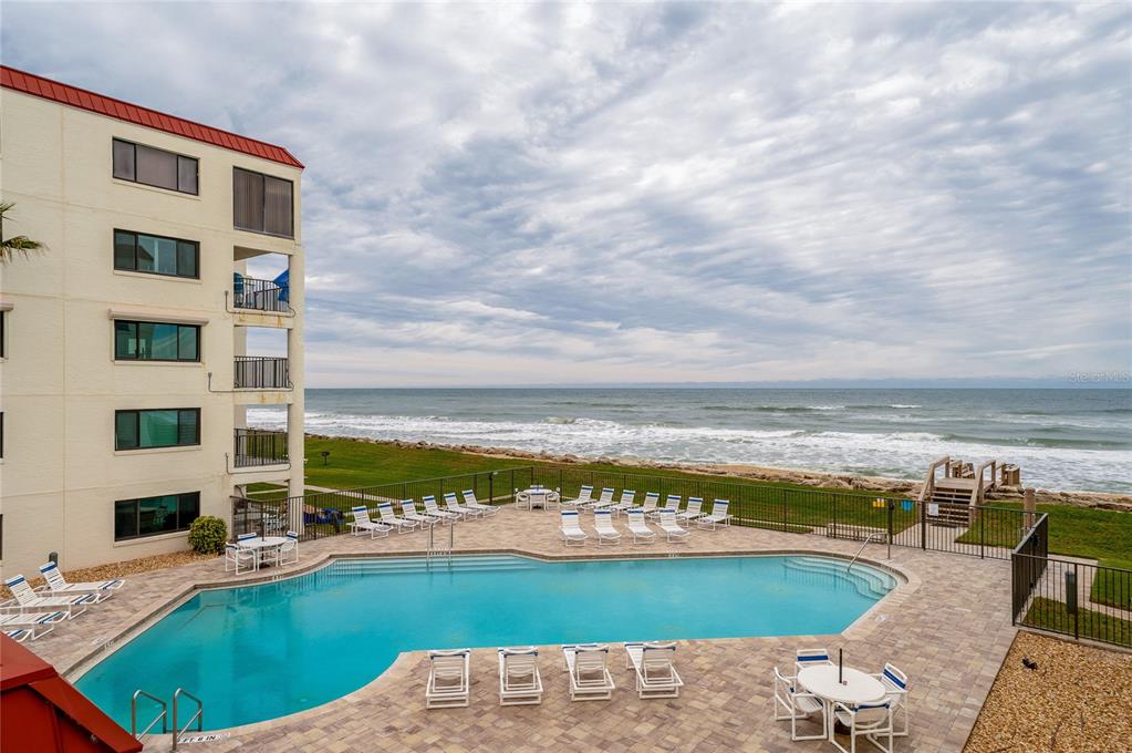 An outdoor swimming pool sits on a patio beside a multi-story building overlooking the ocean — 6727 TURTLEMOUND ROAD UNIT 315, NEW SMYRNA BEACH, FL