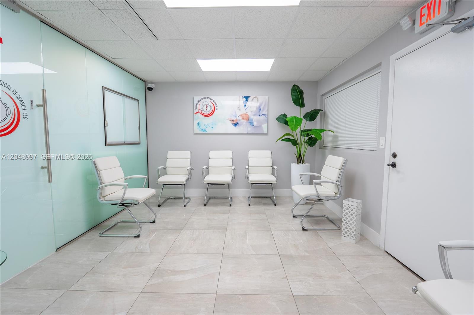 A waiting room features white chairs, tiled floors, a glass wall, and a corporate sign — 747 Ponce De Leon Blvd # 402, Coral Gables FL 33134, CORAL GABLES, FL