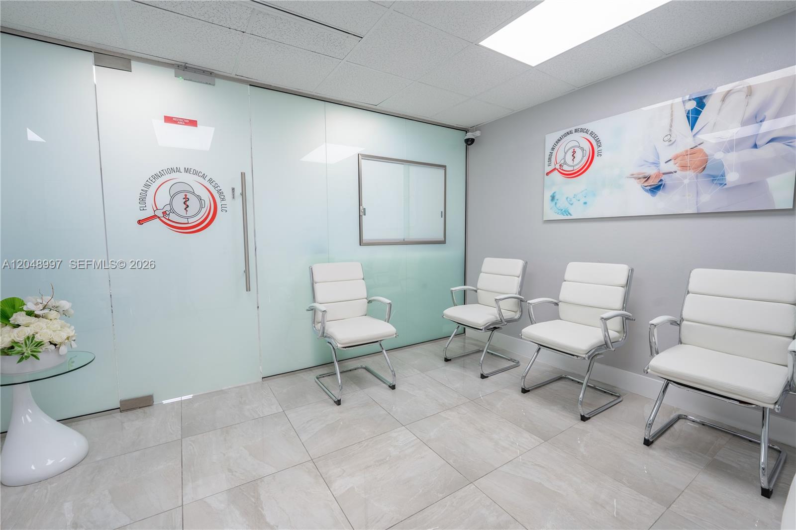 A waiting room features four white chairs, a glass door, and a wall-mounted medical poster — 747 Ponce De Leon Blvd # 402, Coral Gables FL 33134, CORAL GABLES, FL