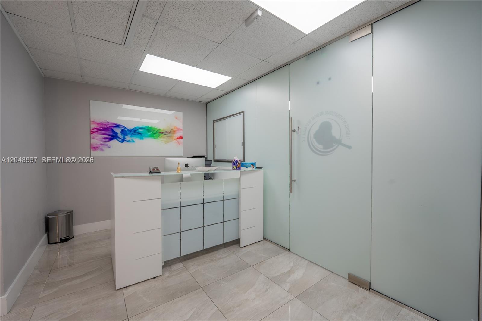 A modern office reception area features a white desk, frosted glass doors, and tiled flooring — 747 Ponce De Leon Blvd # 402, Coral Gables FL 33134, CORAL GABLES, FL