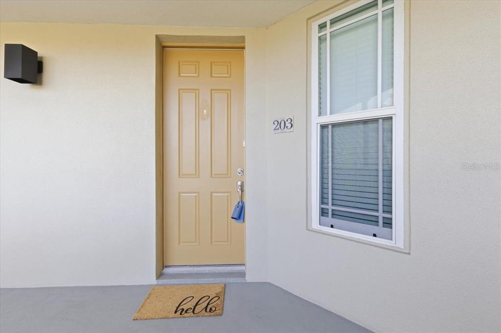 A tan front door with a "hello" mat and a window on a beige wall — 10045 LINKS LANE UNIT 203, ROTONDA WEST, FL