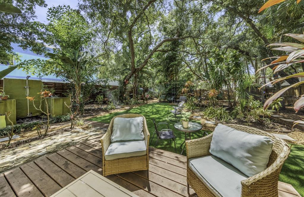 A wooden deck with wicker chairs overlooks a backyard garden with trees and artificial turf — 416 N WASHINGTON AVENUE, CLEARWATER, FL