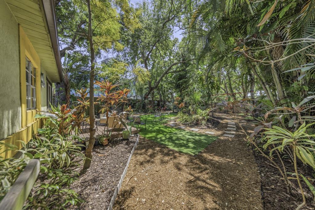 A backyard features a wooden deck, artificial turf, a mulch path, and lush tropical landscaping — 416 N WASHINGTON AVENUE, CLEARWATER, FL