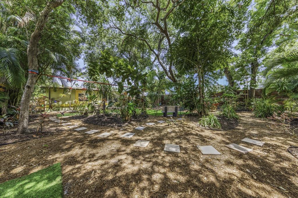 A backyard features a stone paver path, mature trees, and a small wooden bench — 416 N WASHINGTON AVENUE, CLEARWATER, FL