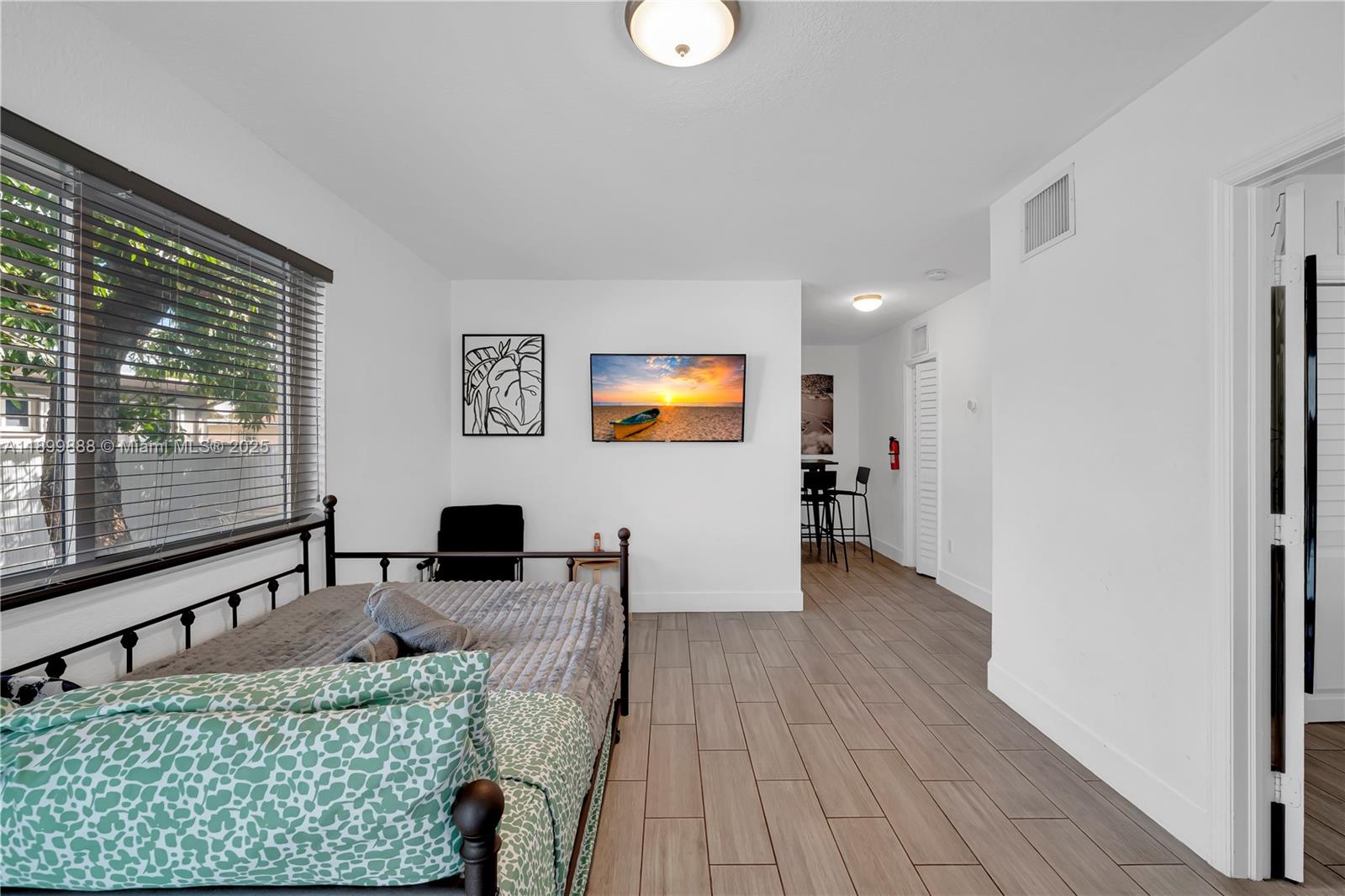 A bedroom features a metal bed frame, wood-look tile flooring, and a wall-mounted television — 3181 NW 5th Ave, Miami FL 33127, MIAMI, FL