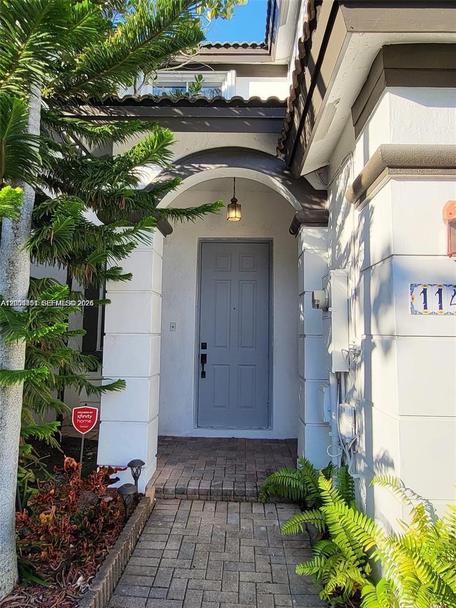 A gray front door is set within a white arched entryway with brick pavers — 11425 NW 76th Ter, Doral FL 33178, DORAL, FL
