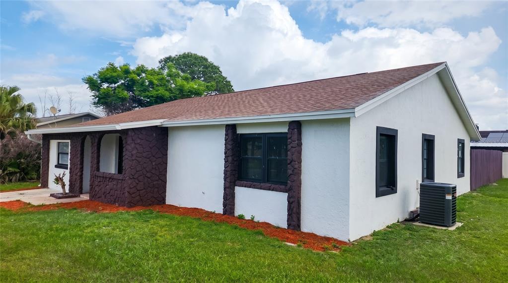 A white single-story house with dark stone accents and black-framed windows sits on a lawn — 107 IGUALA DRIVE, KISSIMMEE, FL