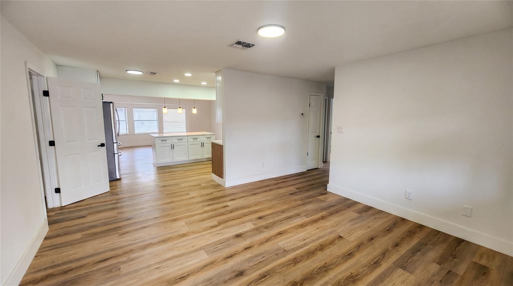 A bright room with wood-look flooring leads into a kitchen featuring white cabinets and lighting — 107 IGUALA DRIVE, KISSIMMEE, FL