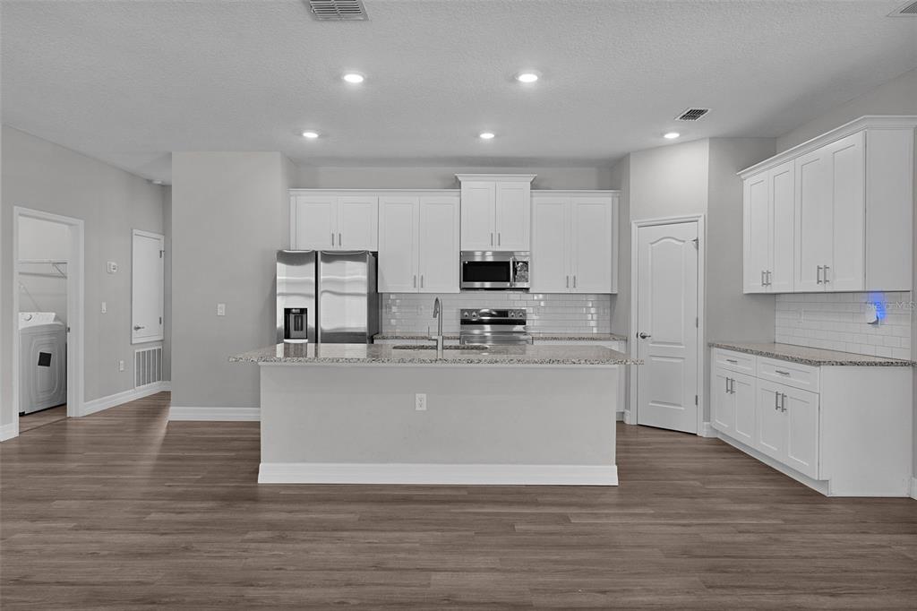 A modern kitchen features white cabinetry, stainless steel appliances, a granite island, and wood flooring — 8578 SE 164TH PLACE, SUMMERFIELD, FL