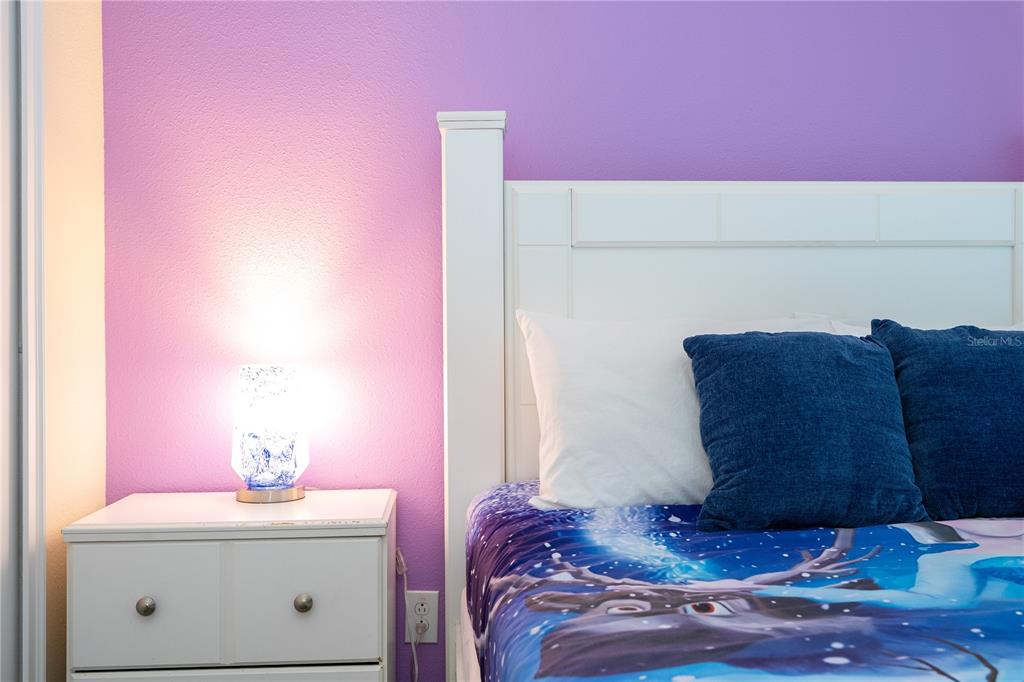 A bedroom features a white nightstand, a lit lamp, and a bed with blue bedding — 4908 CLOCK TOWER DRIVE, KISSIMMEE, FL