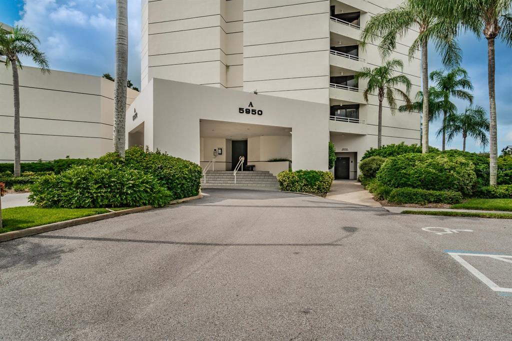 The exterior of a multi-story residential building features a covered entrance marked with the number 5950 — 5950 PELICAN BAY PLAZA S UNIT 705, GULFPORT, FL