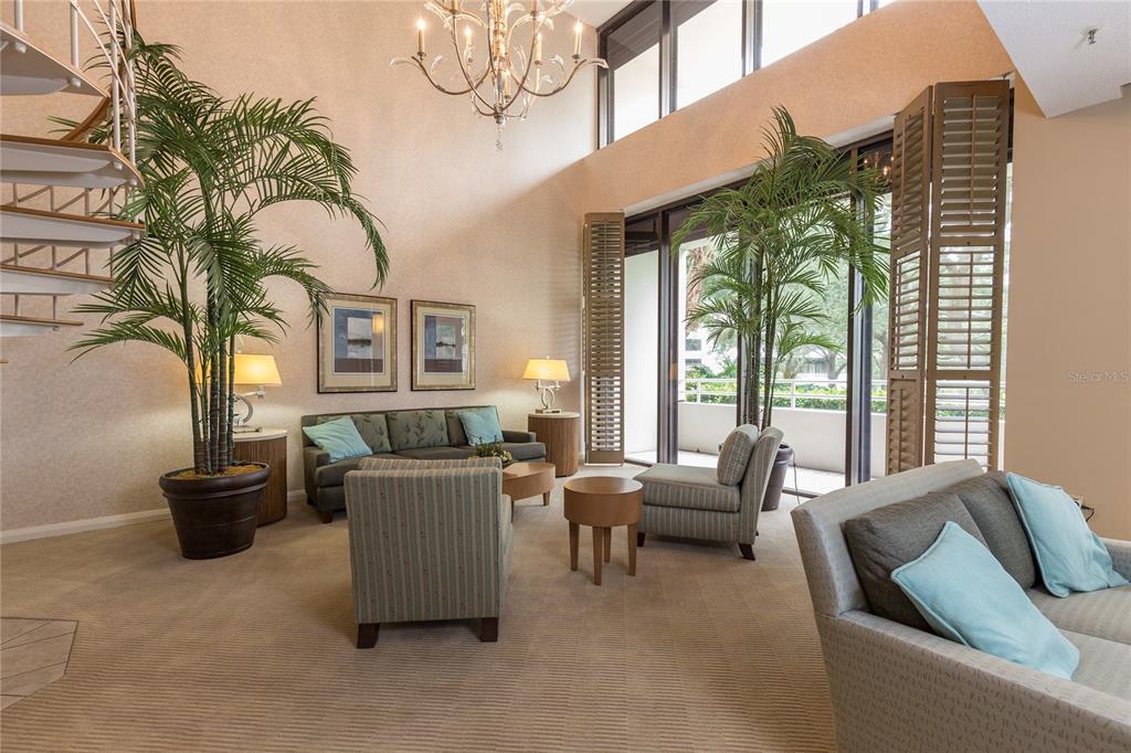 A spacious living room features high ceilings, a spiral staircase, large windows, and potted palms — 5950 PELICAN BAY PLAZA S UNIT 705, GULFPORT, FL