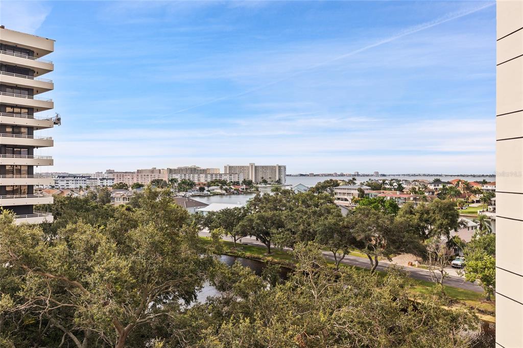 An elevated view of a coastal neighborhood with a canal, trees, and distant apartment buildings — 5950 PELICAN BAY PLAZA S UNIT 705, GULFPORT, FL