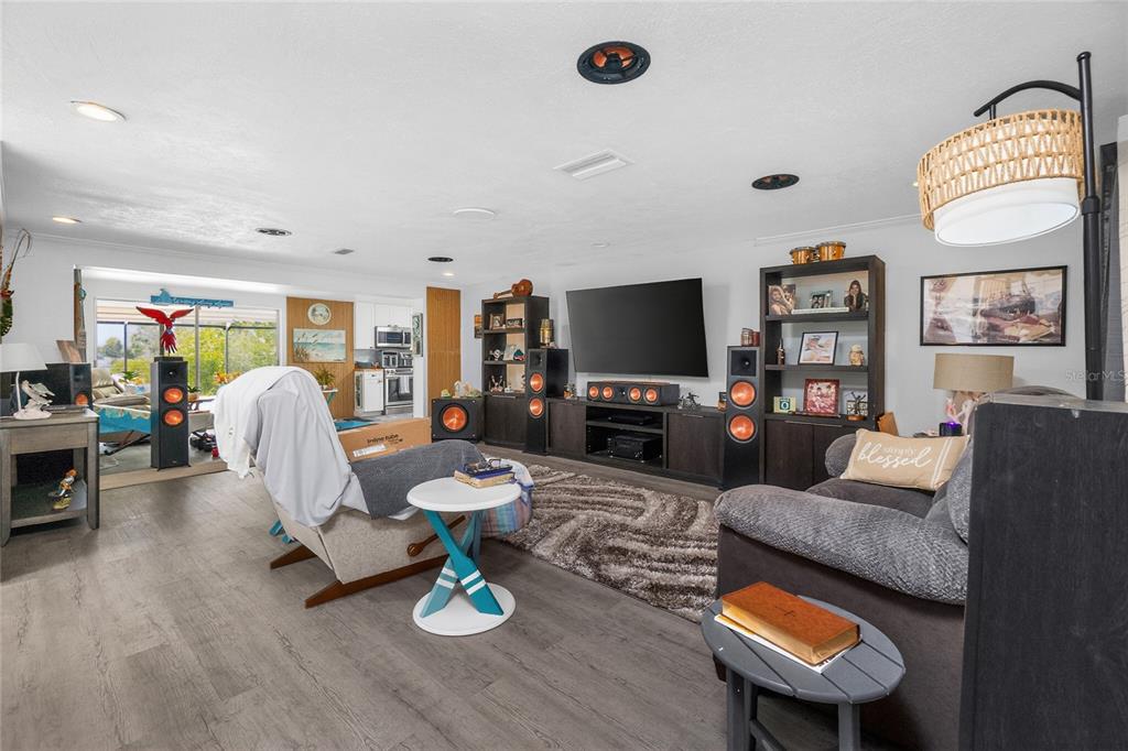 A living room features wood-look flooring, a large television, and a view into the kitchen — 625 SANDPIPER LANE, NOKOMIS, FL