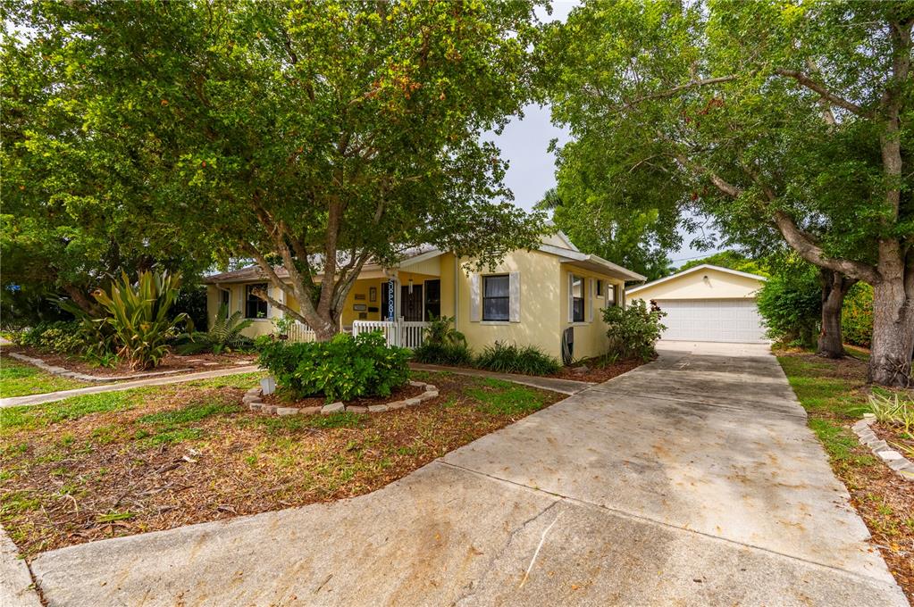 A yellow single-story house with a white front porch, concrete driveway, and large shade trees — 311 GILL STREET, PUNTA GORDA, FL
