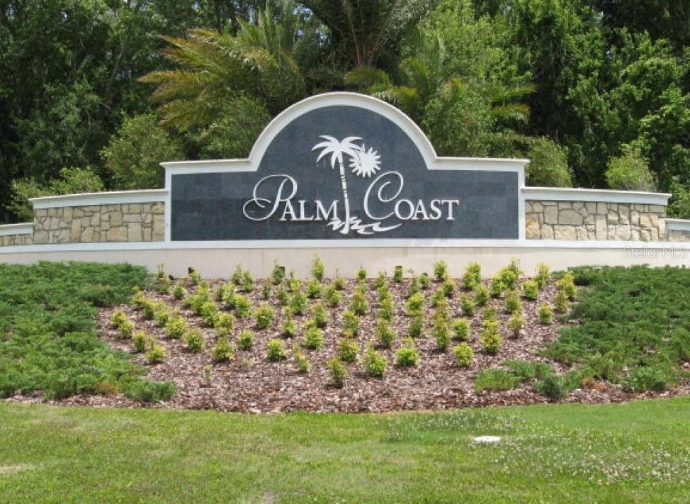 A stone and dark panel monument sign reads Palm Coast in front of landscaped greenery — 70 BUTTERMILL DRIVE, PALM COAST, FL