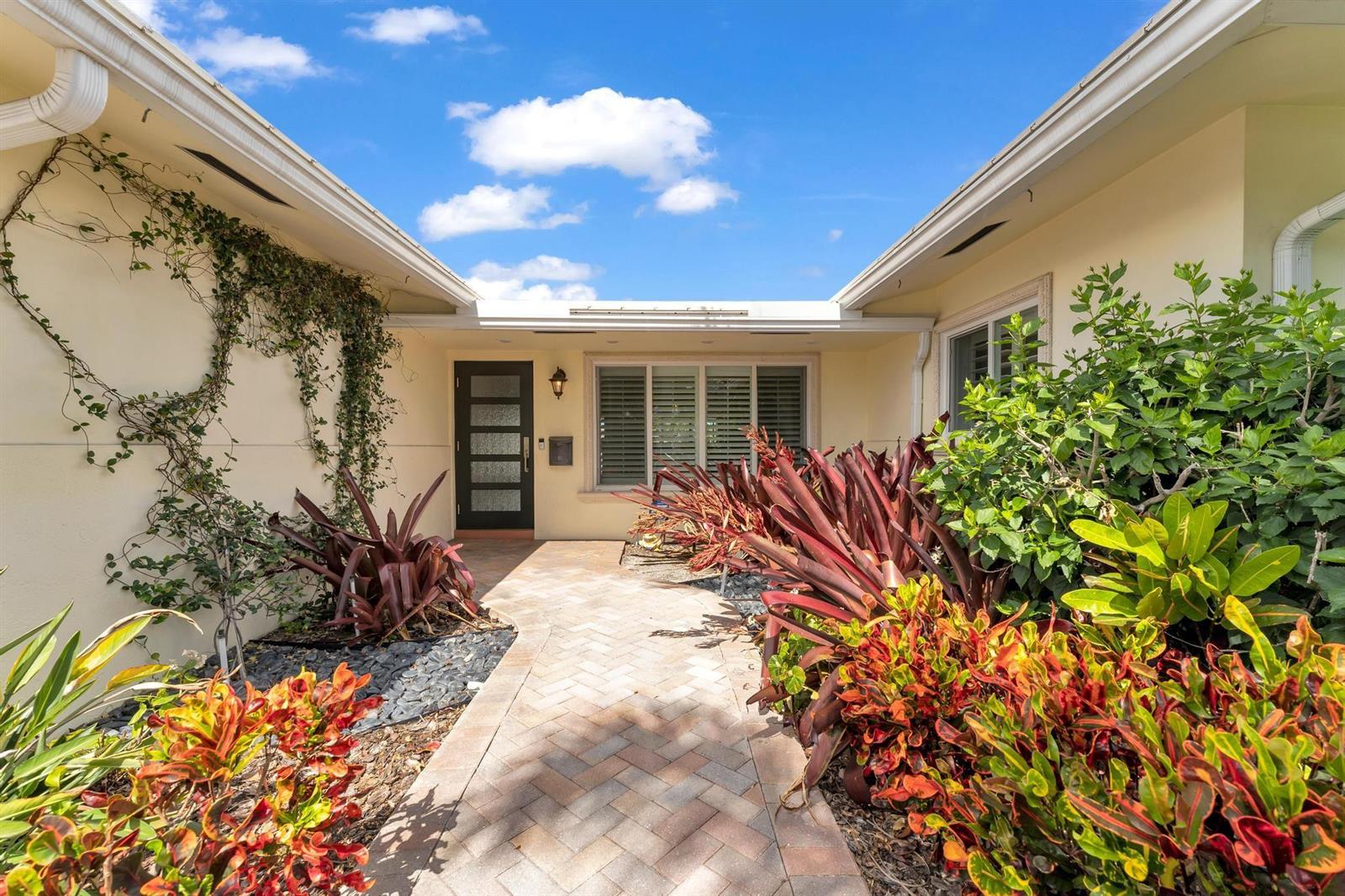 A paved walkway leads to the front entrance of a house with lush tropical landscaping — 925 SE 10th Street, Pompano Beach FL 33060, POMPANO BEACH, FL