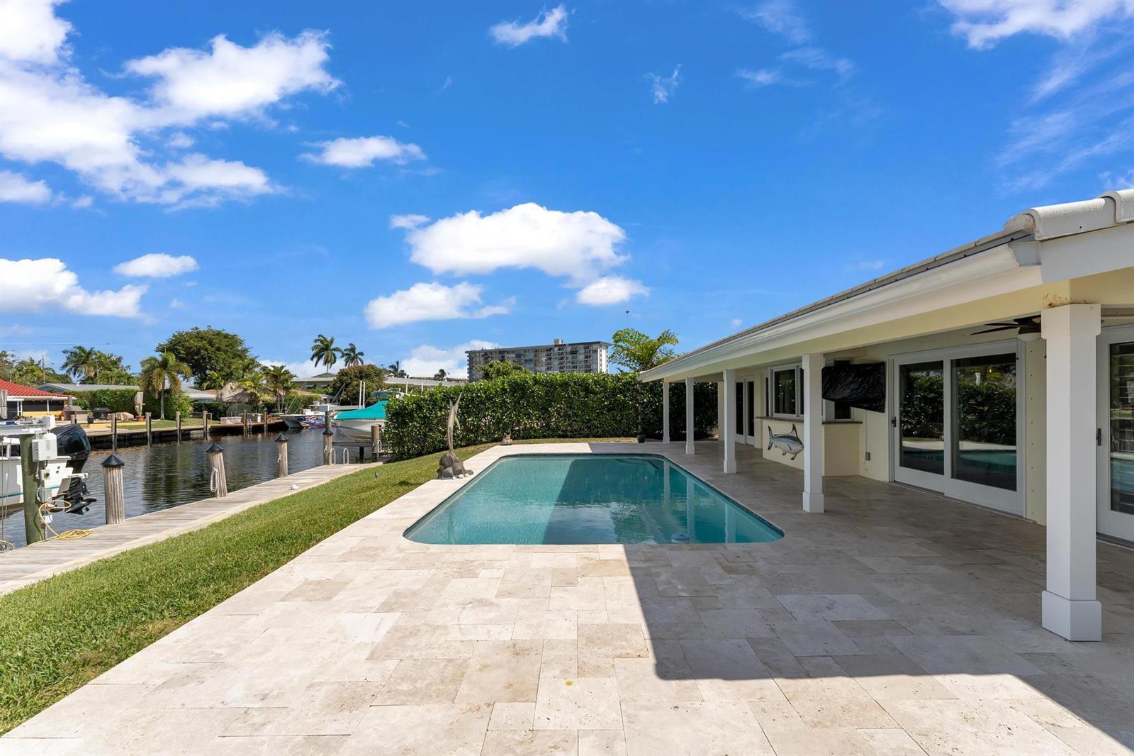 A backyard swimming pool sits on a stone patio next to a canal with boats — 925 SE 10th Street, Pompano Beach FL 33060, POMPANO BEACH, FL