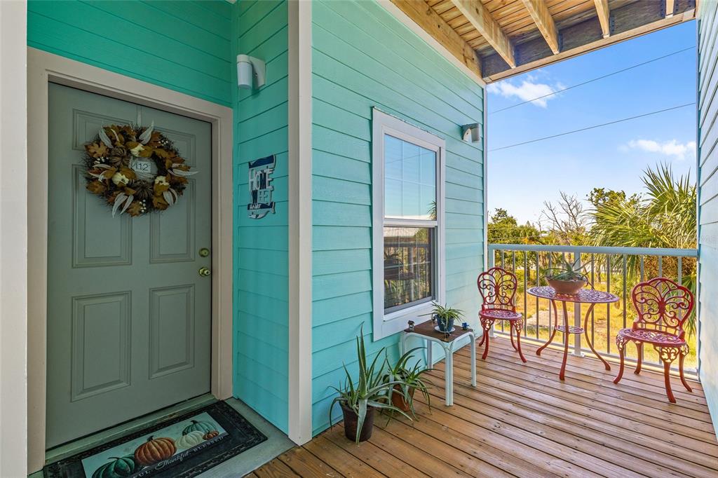 A teal-sided porch features a front door with a wreath, wooden flooring, and patio furniture — 502 MAIN STREET UNIT 112, HORSESHOE BEACH, FL
