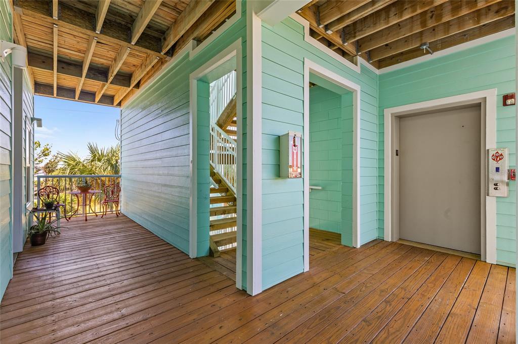 A covered wooden deck features a staircase, an elevator, and a small outdoor seating area — 502 MAIN STREET UNIT 112, HORSESHOE BEACH, FL