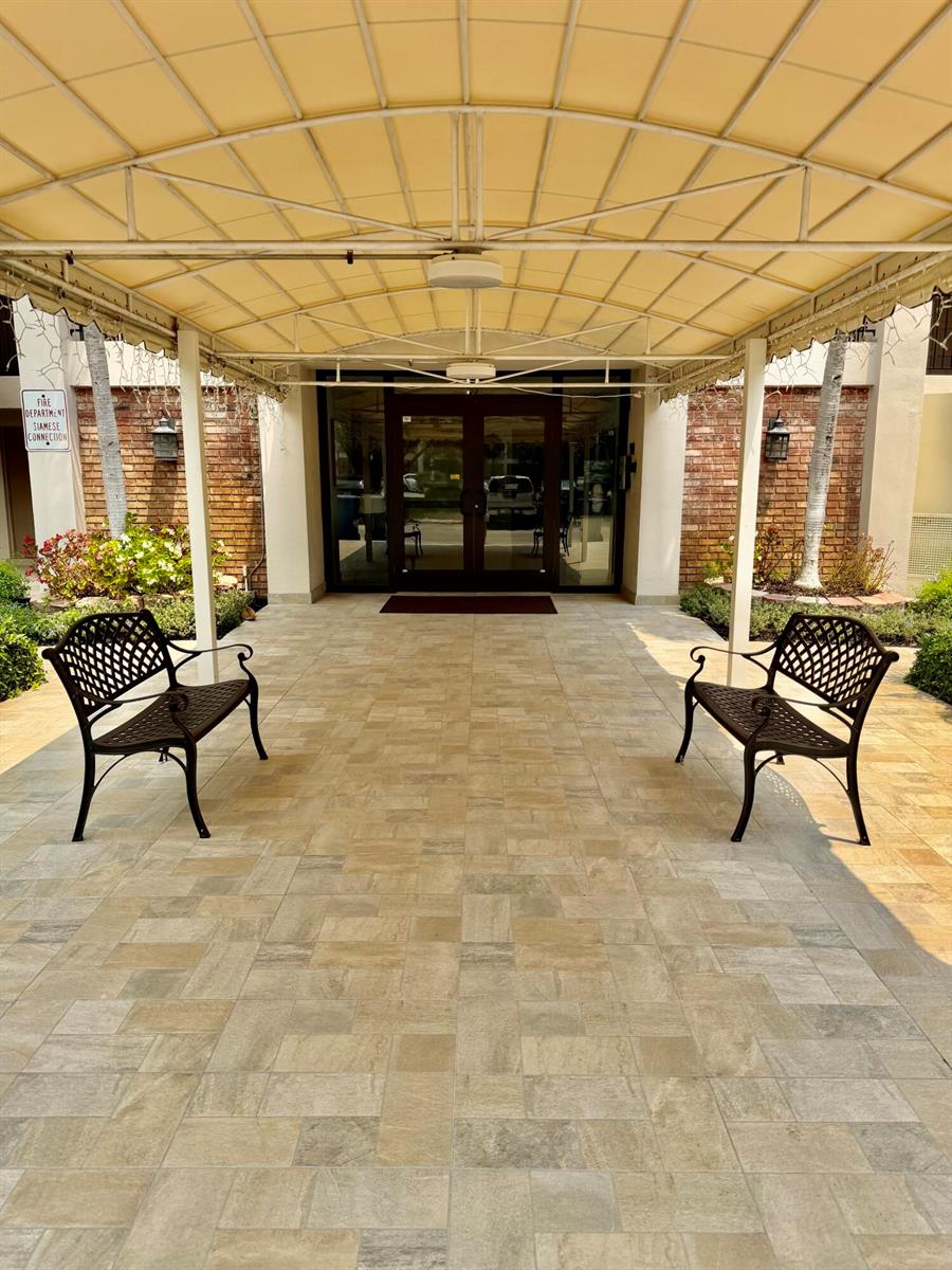 A covered outdoor entryway features two metal benches on a paved patio before glass doors — 2801 N Palm Aire Drive # 604, Pompano Beach FL 33069, POMPANO BEACH, FL