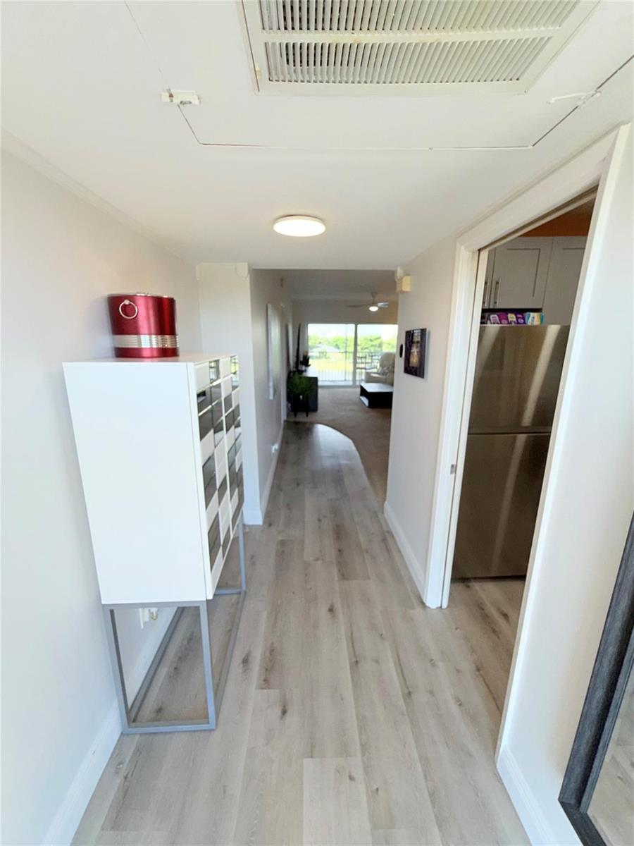 A hallway with light wood-look flooring leads toward a living area with a sliding door — 2801 N Palm Aire Drive # 604, Pompano Beach FL 33069, POMPANO BEACH, FL