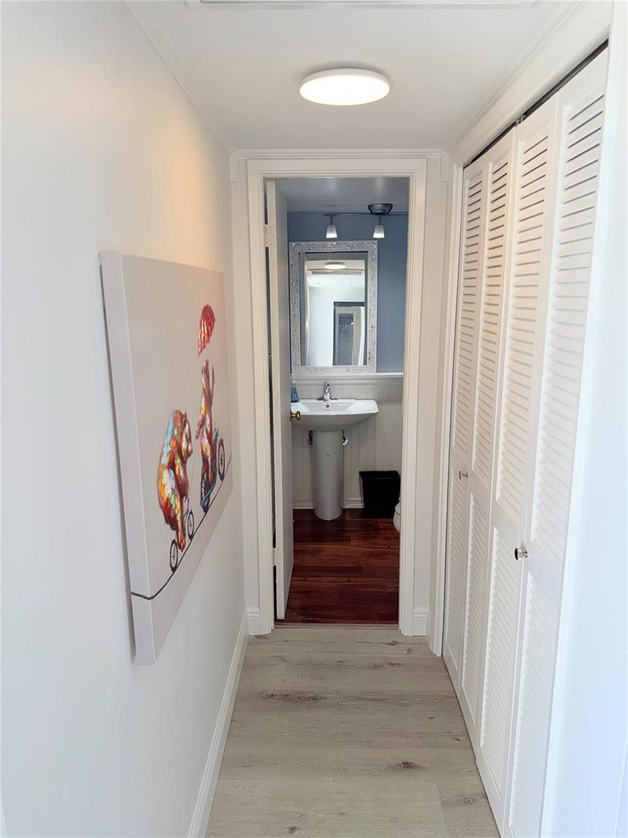 A hallway with light wood-look flooring leads to a bathroom featuring a pedestal sink — 2801 N Palm Aire Drive # 604, Pompano Beach FL 33069, POMPANO BEACH, FL