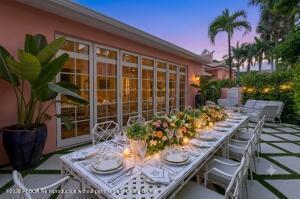An outdoor dining table with floral centerpieces sits on a patio beside a pink house — 142 Peruvian Avenue # 1020, Palm Beach FL 33480, PALM BEACH, FL