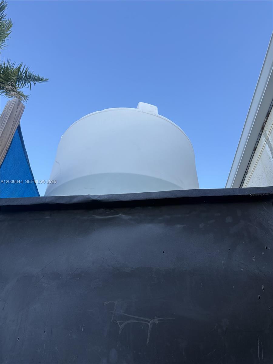A white plastic water storage tank sits behind a black privacy fence under a blue sky — 82 SW 8, Miami FL 33144, MIAMI, FL