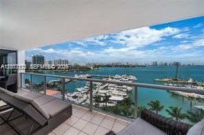 A balcony with lounge furniture overlooks a marina and a distant city skyline — 1900 Sunset Harbour Dr # 1012, Miami Beach FL 33139, MIAMI BEACH, FL