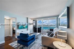 A living room features a blue armchair, a beige sofa, and floor-to-ceiling windows overlooking water — 1900 Sunset Harbour Dr # 1012, Miami Beach FL 33139, MIAMI BEACH, FL