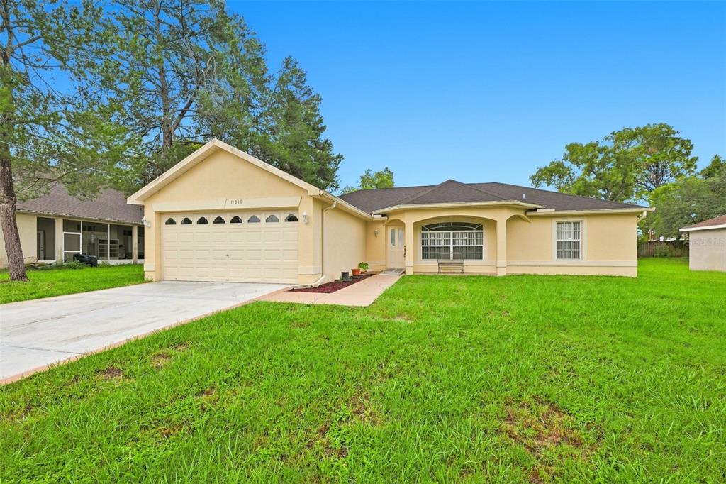 A single-story house with a beige stucco exterior, a two-car garage, and a grassy lawn — 11048 RED COACH STREET, SPRING HILL, FL