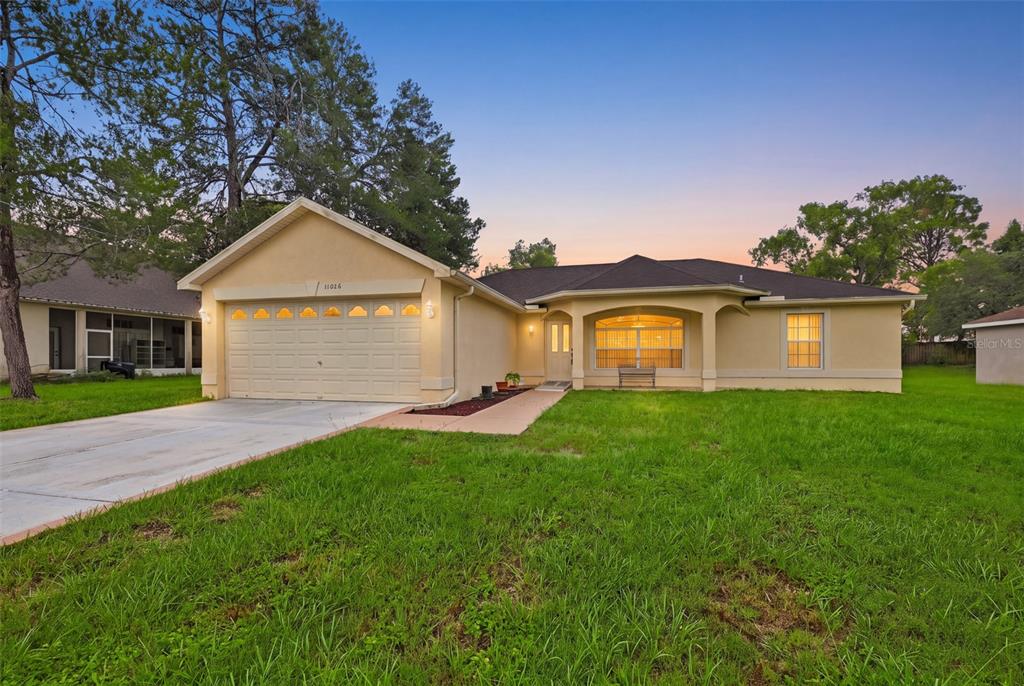 A single-story house with a beige stucco exterior, a two-car garage, and a front lawn — 11048 RED COACH STREET, SPRING HILL, FL