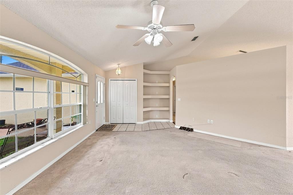 A living room features beige carpet, a vaulted ceiling with a fan, and built-in wall shelves — 11048 RED COACH STREET, SPRING HILL, FL