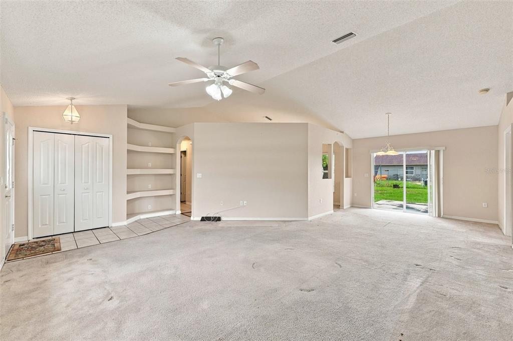 A spacious living room features beige carpeting, a vaulted ceiling with a fan, and built-in shelves — 11048 RED COACH STREET, SPRING HILL, FL