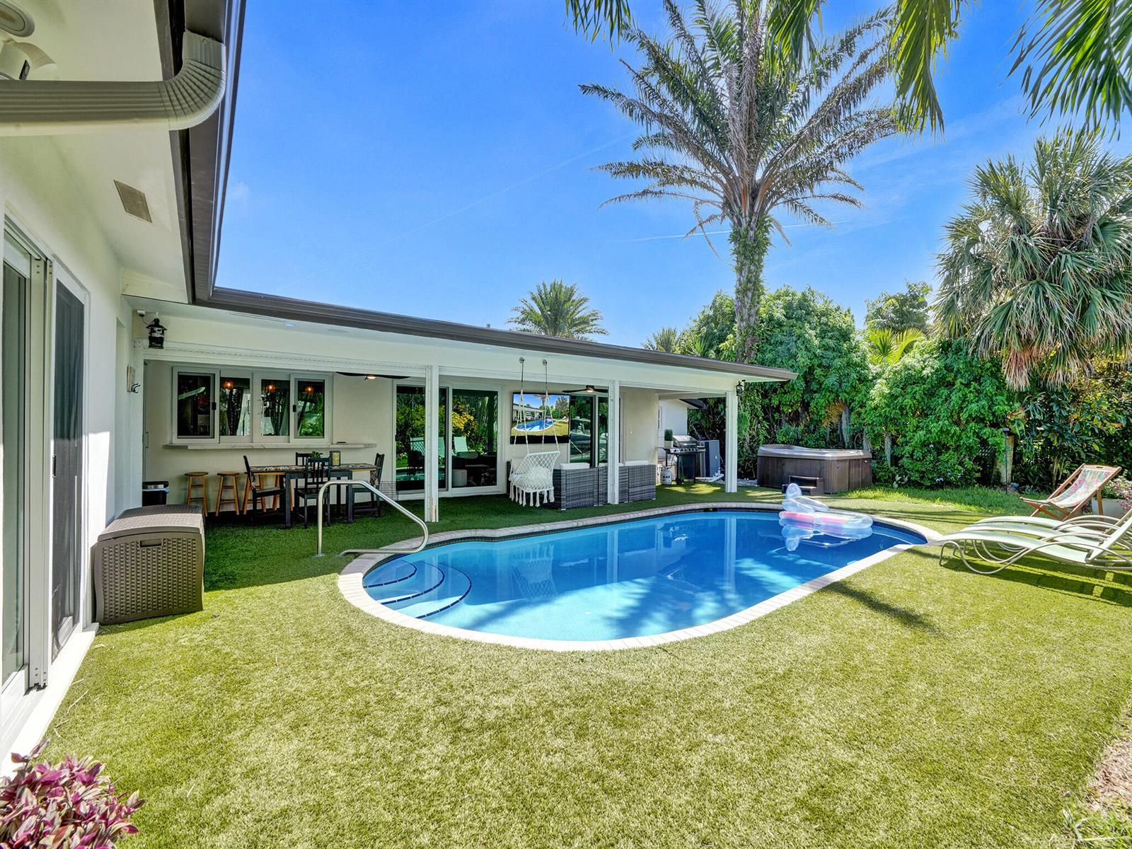 A backyard features a swimming pool, artificial turf, a covered patio, and a hot tub — 3821 NE 29th Avenue, Lighthouse Point FL 33064, LIGHTHOUSE POINT, FL