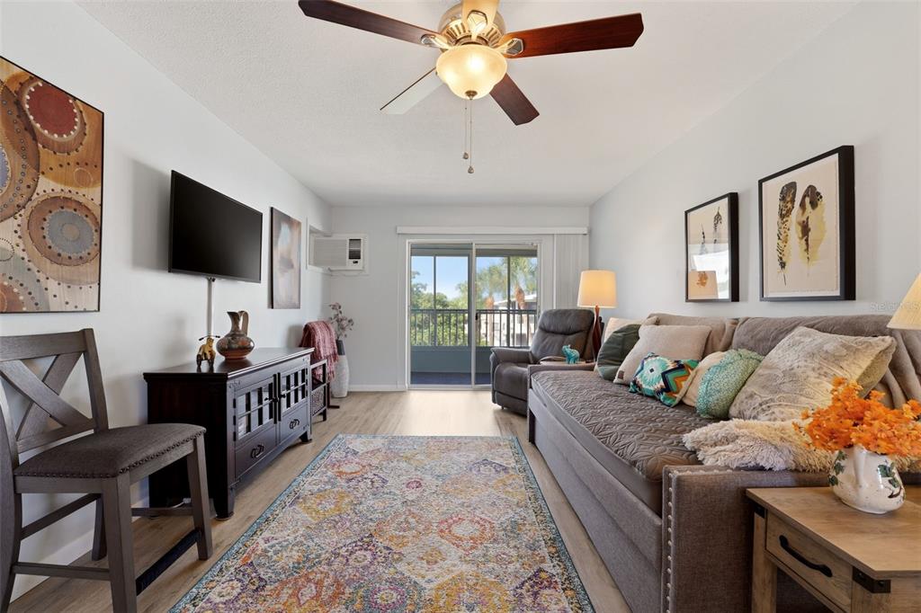 A living room features light wood flooring, a ceiling fan, a television, and a balcony — 2545 FLAMINGO BOULEVARD UNIT L37, BRADENTON, FL