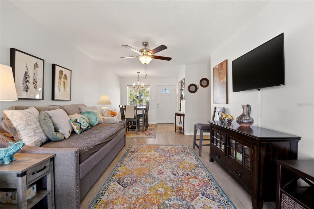 A living room features a grey sofa, patterned area rug, ceiling fan, and sliding glass doors — 2545 FLAMINGO BOULEVARD UNIT L37, BRADENTON, FL