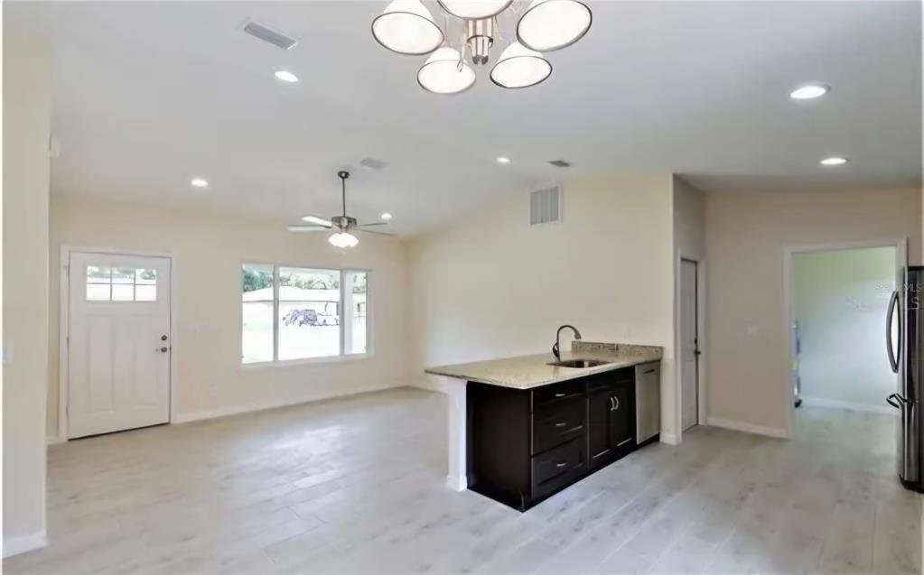 An open-concept kitchen and living area features light wood-look tile floors and dark cabinetry — 16295 SW 28TH COURT, OCALA, FL